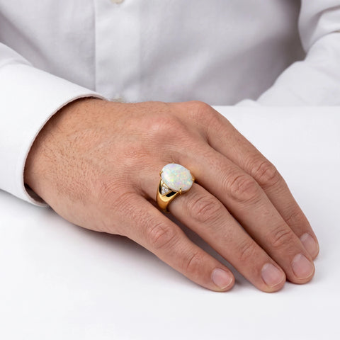 Man wearing a gold ring with an opal stone on a white background