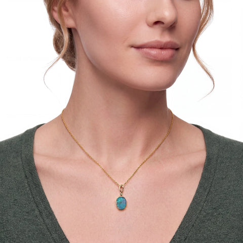 Woman wearing a gold necklace with a turquoise pendant on a white background