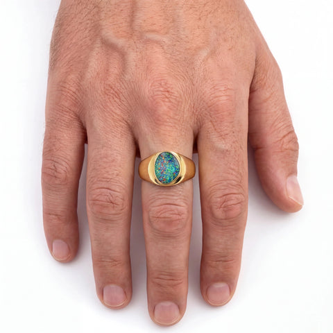 Gold ring with a colourful gemstone on a person's finger against a white background