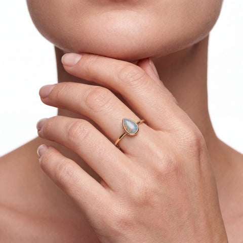 Woman wearing a ring with a teardrop-shaped gemstone on a neutral background