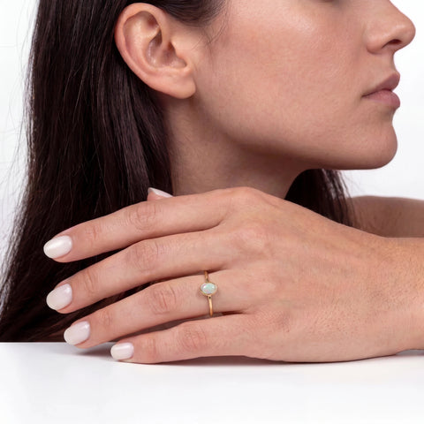 Close-up of a woman's hand wearing a gold ring with an opal stone, on a neutral background.