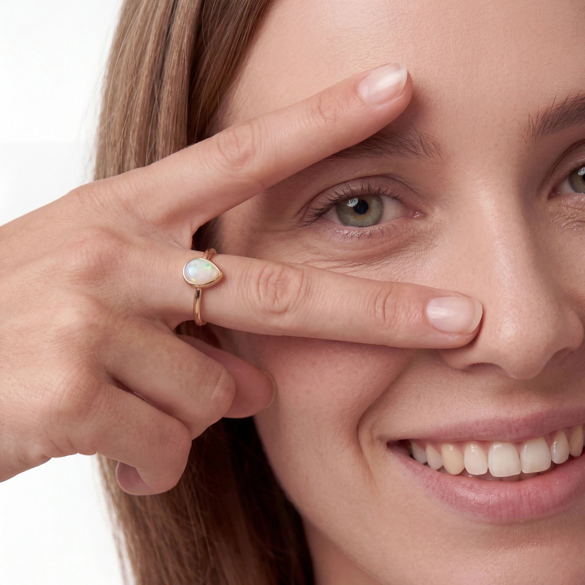 Woman wearing a gold ring with a heart-shaped gemstone, smiling.