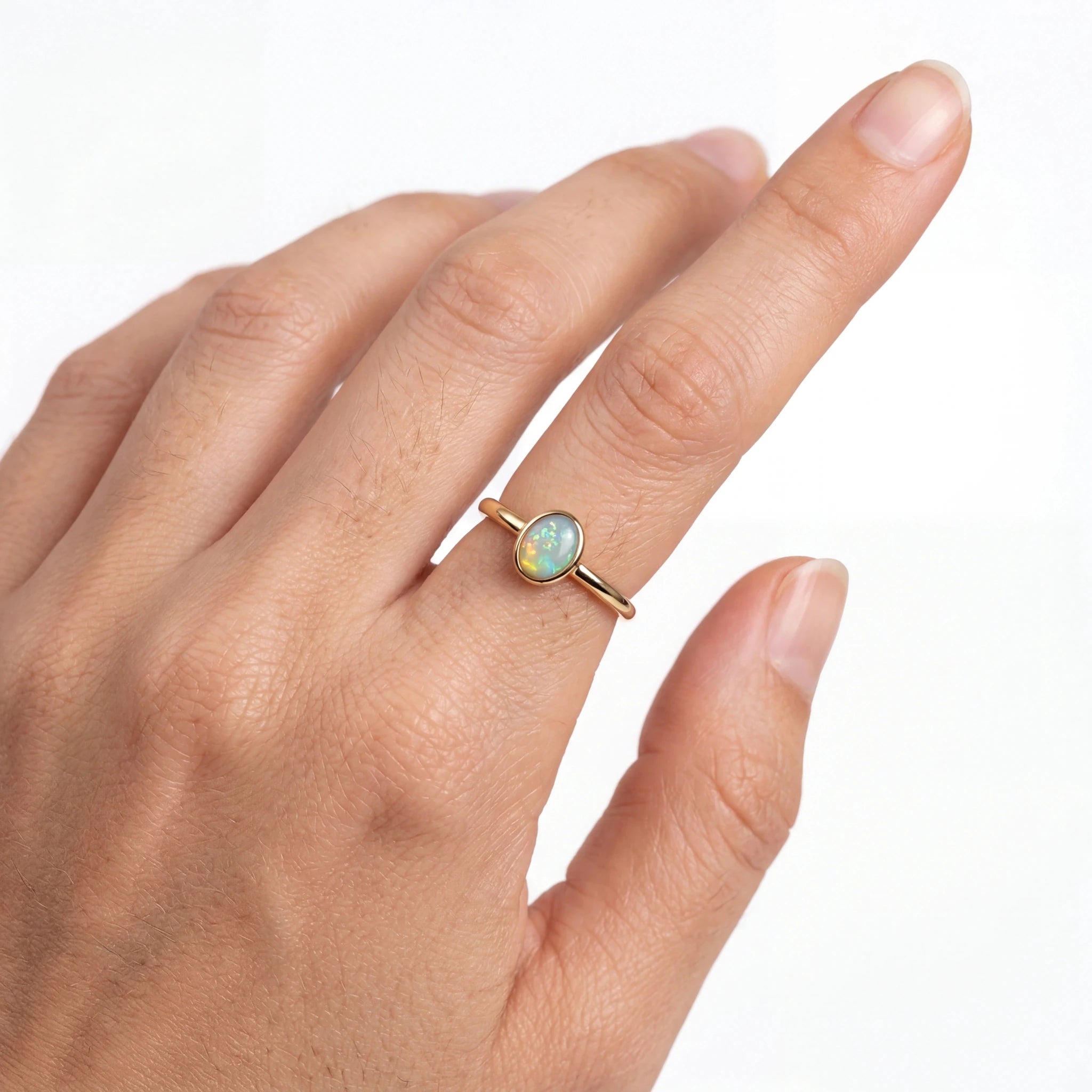 Gold ring with an opal stone on a hand against a white background