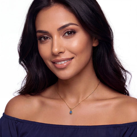 Woman wearing a blue off-shoulder top and gold necklace with a blue pendant on a white background
