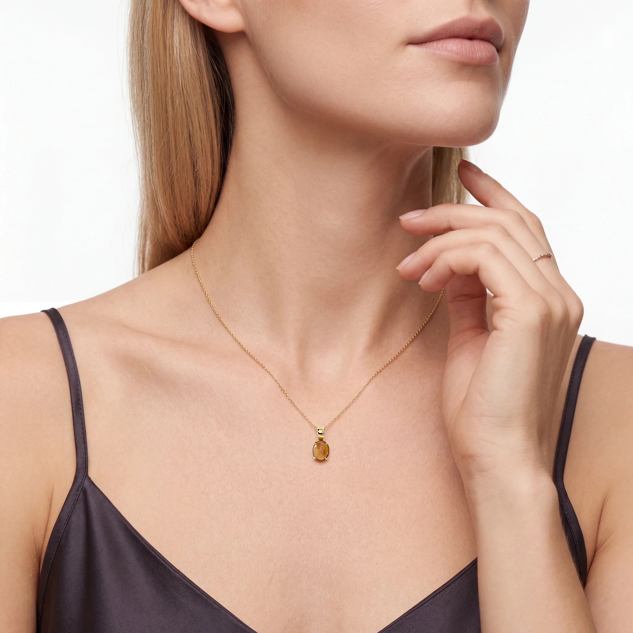 Woman wearing a gold necklace with a pendant on a plain background