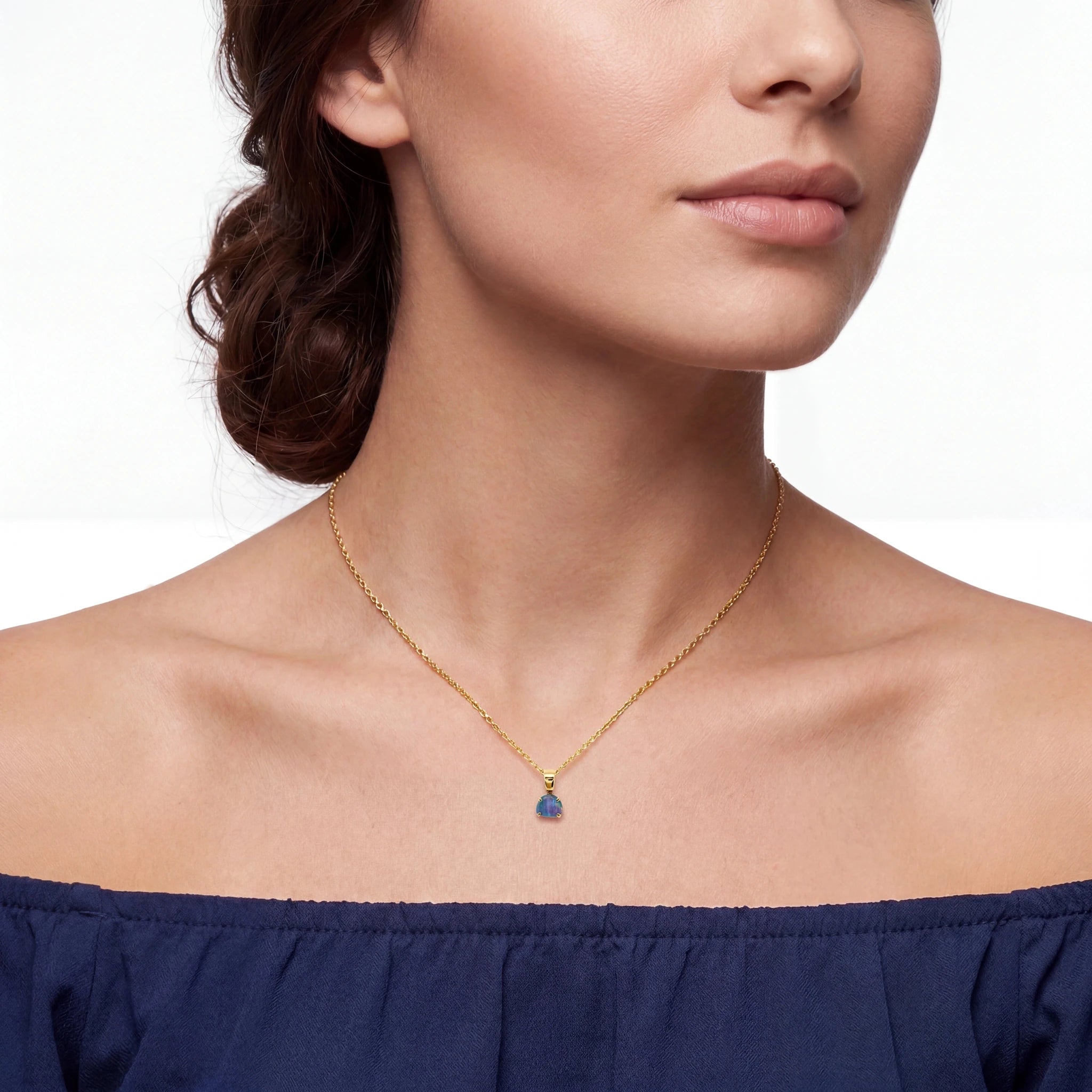 Woman wearing a gold necklace with a blue pendant on a white background