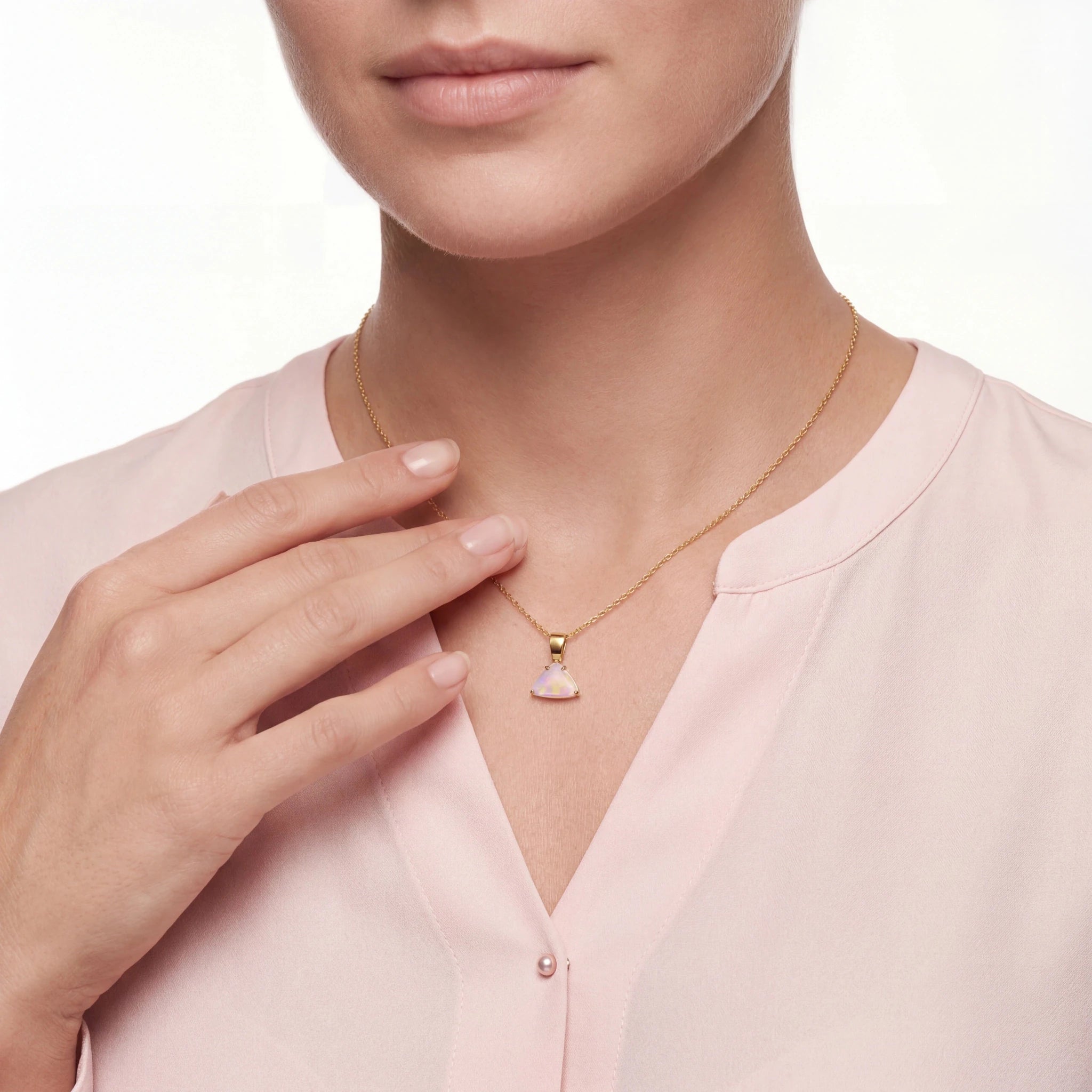 Person wearing a gold necklace with a heart-shaped pendant, set against a soft pink background.