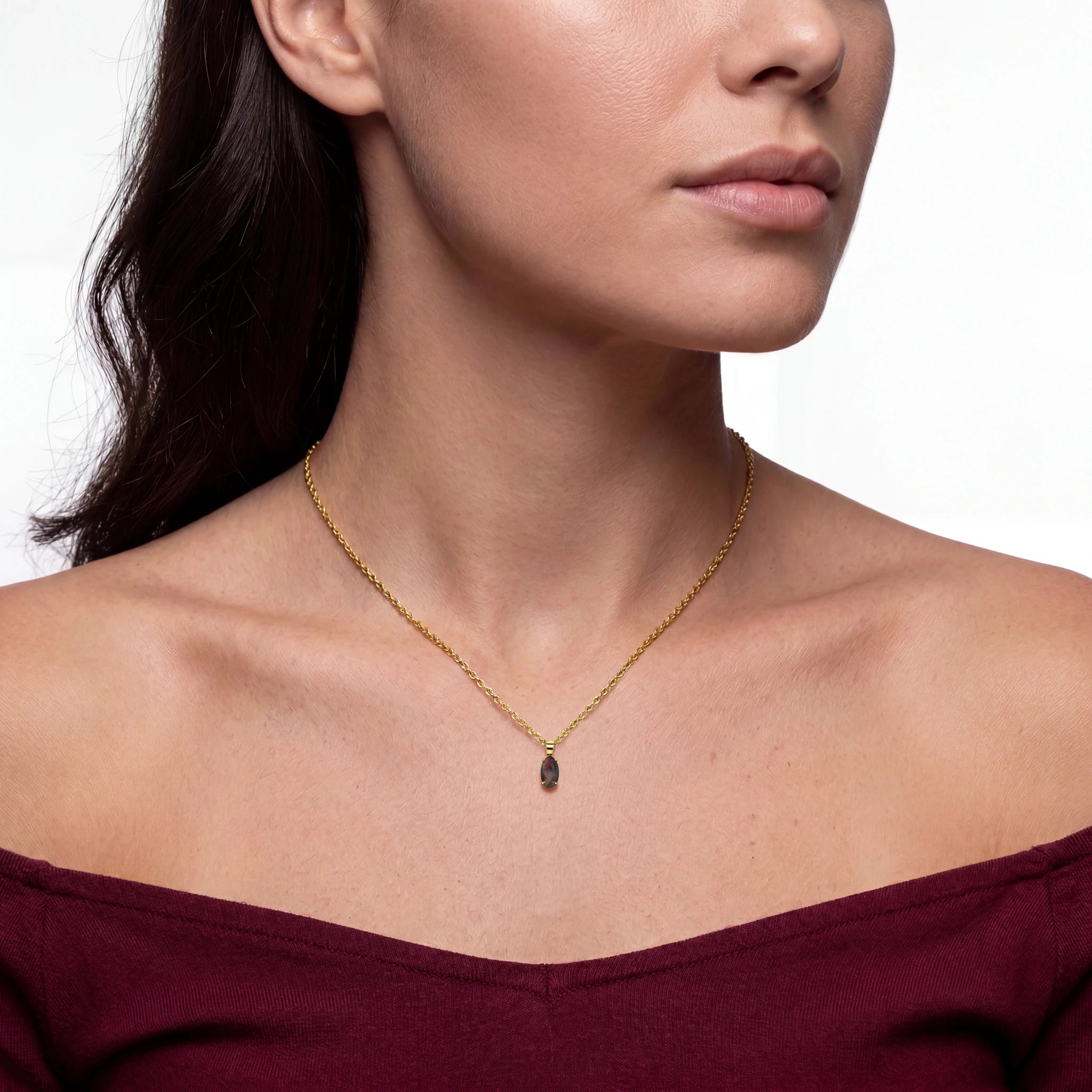 Woman wearing a gold necklace with a maroon top on a neutral background