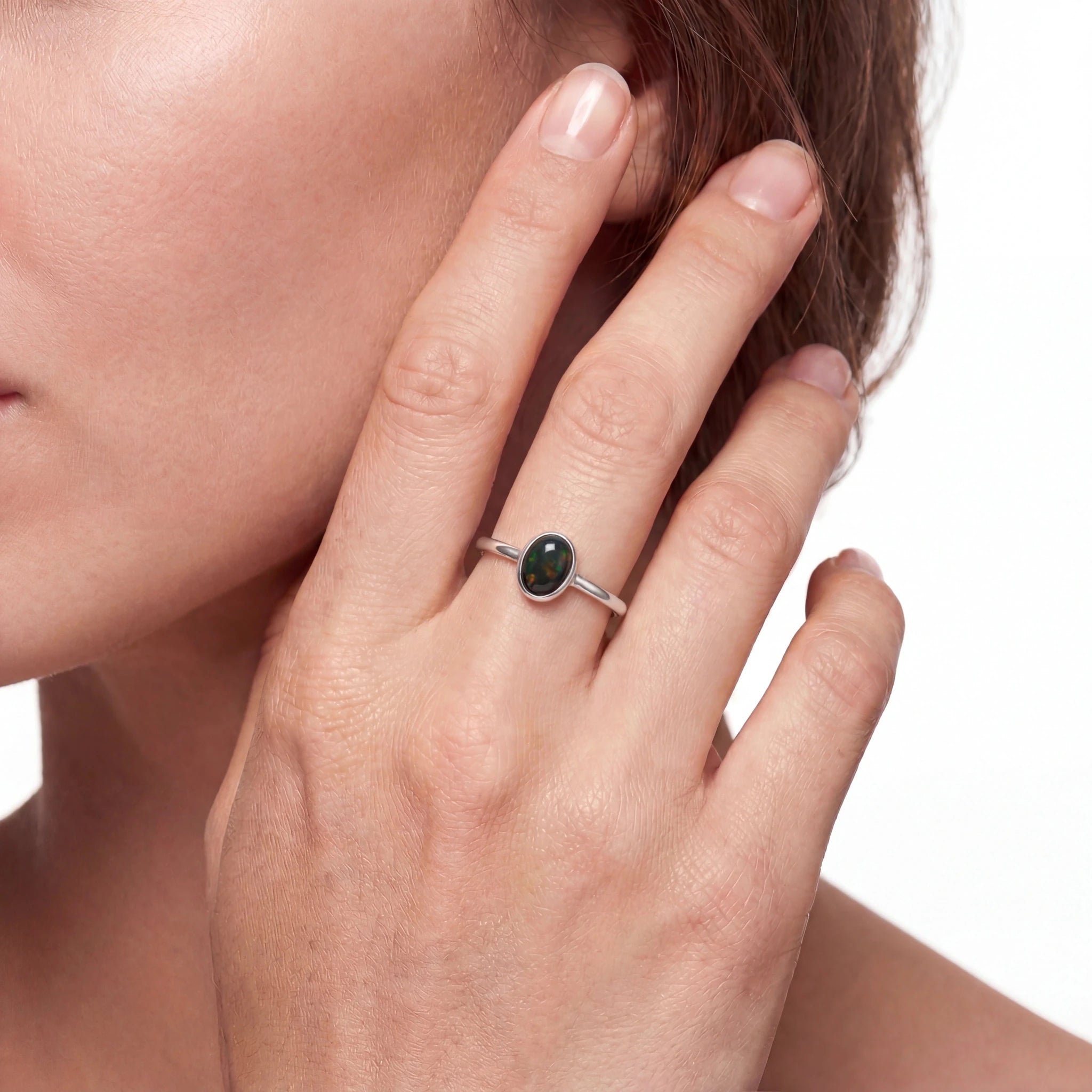 Close-up of a hand wearing a silver ring with a green gemstone, against a neutral background.