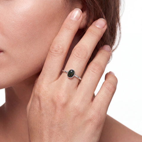 Close-up of a hand wearing a silver ring with a green gemstone, against a neutral background.