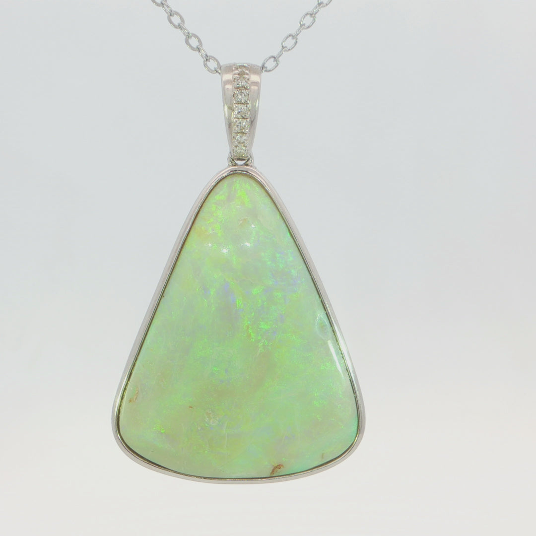 Video of a silver pendant necklace featuring a large, teardrop-shaped green opal gemstone with iridescent flashes, set in a silver bezel with a small row of clear stones at the top