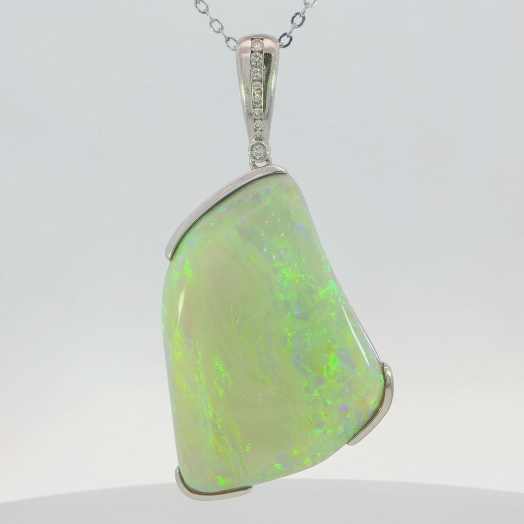 Video of a silver pendant necklace featuring a large, irregularly shaped white opal gemstone with vibrant green and orange flashes, set in a polished silver bezel with a diamond-accented bail