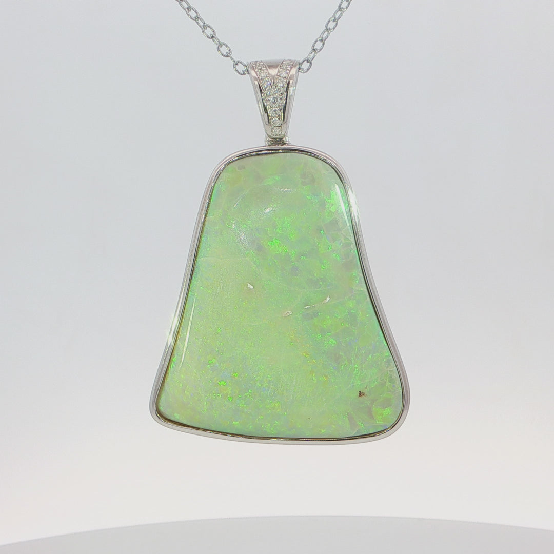 Video of a silver pendant necklace featuring a large, irregular-shaped green opal gemstone with vibrant iridescent flashes, suspended from a silver chain with a small crystal-accented bail.
