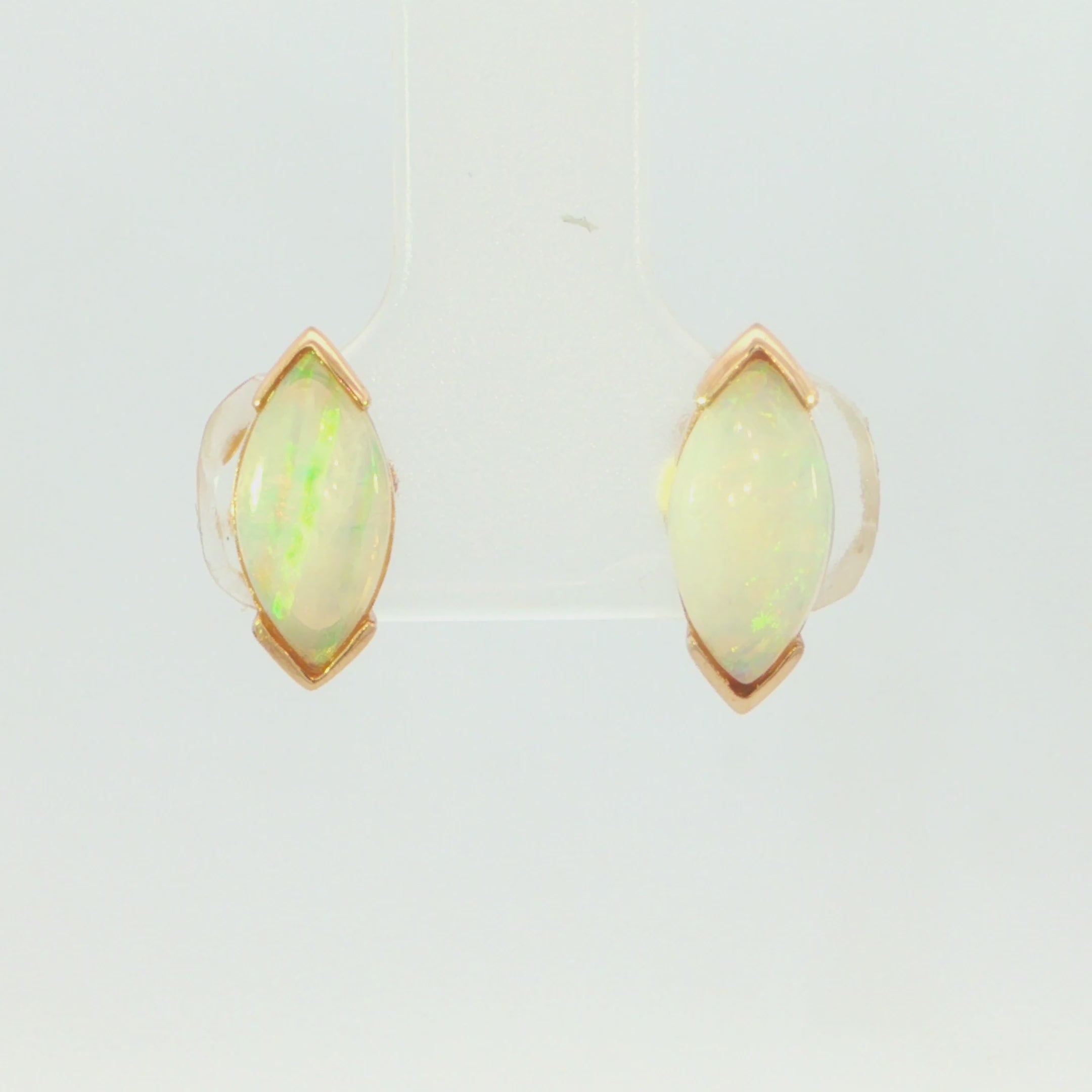 Video of a pair of gold stud earrings featuring marquise-cut white opal gemstones in a prong setting