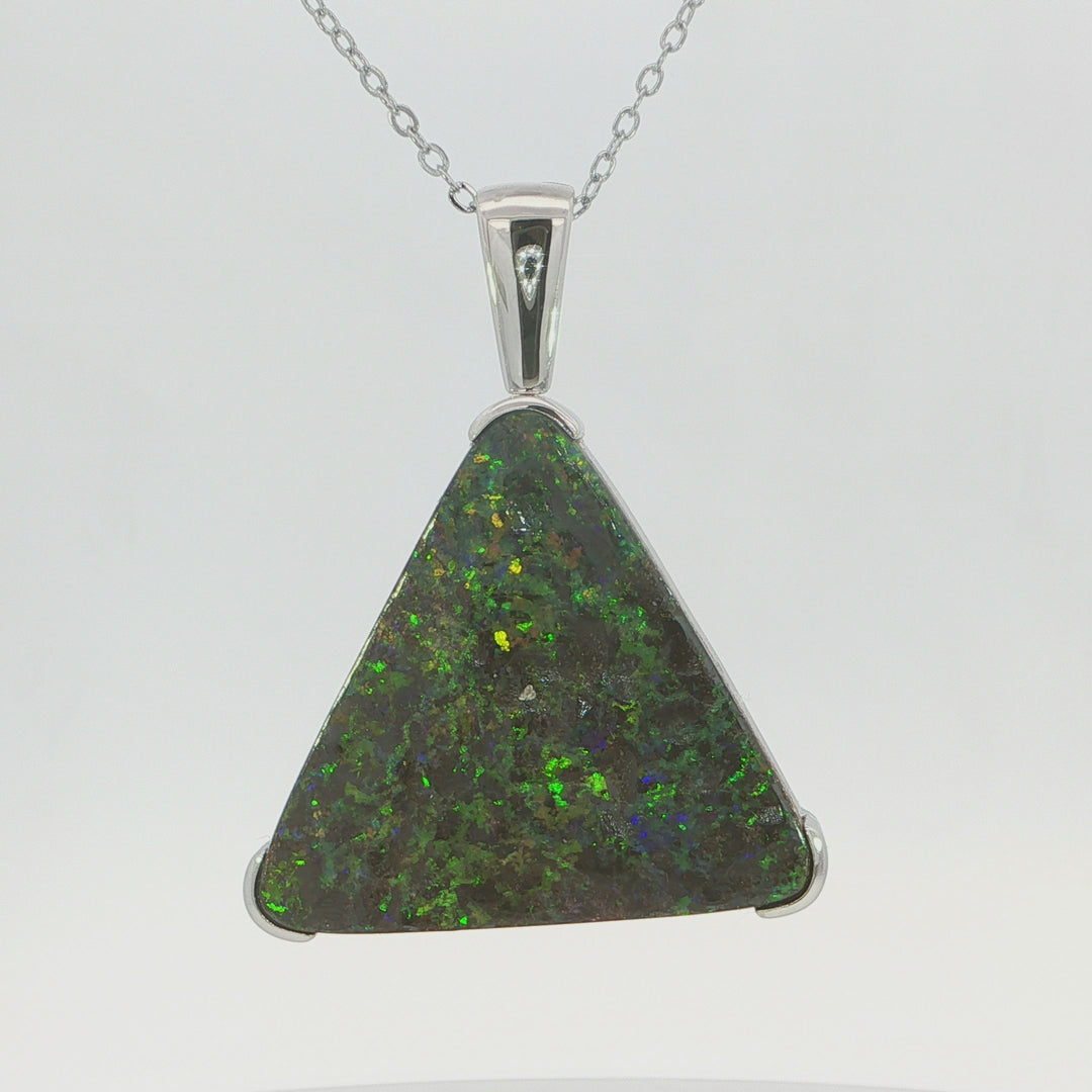Video of a silver triangle pendant necklace featuring a vibrant green opal stone with iridescent flashes, set in a polished silver bezel with a textured brown inlay on the side