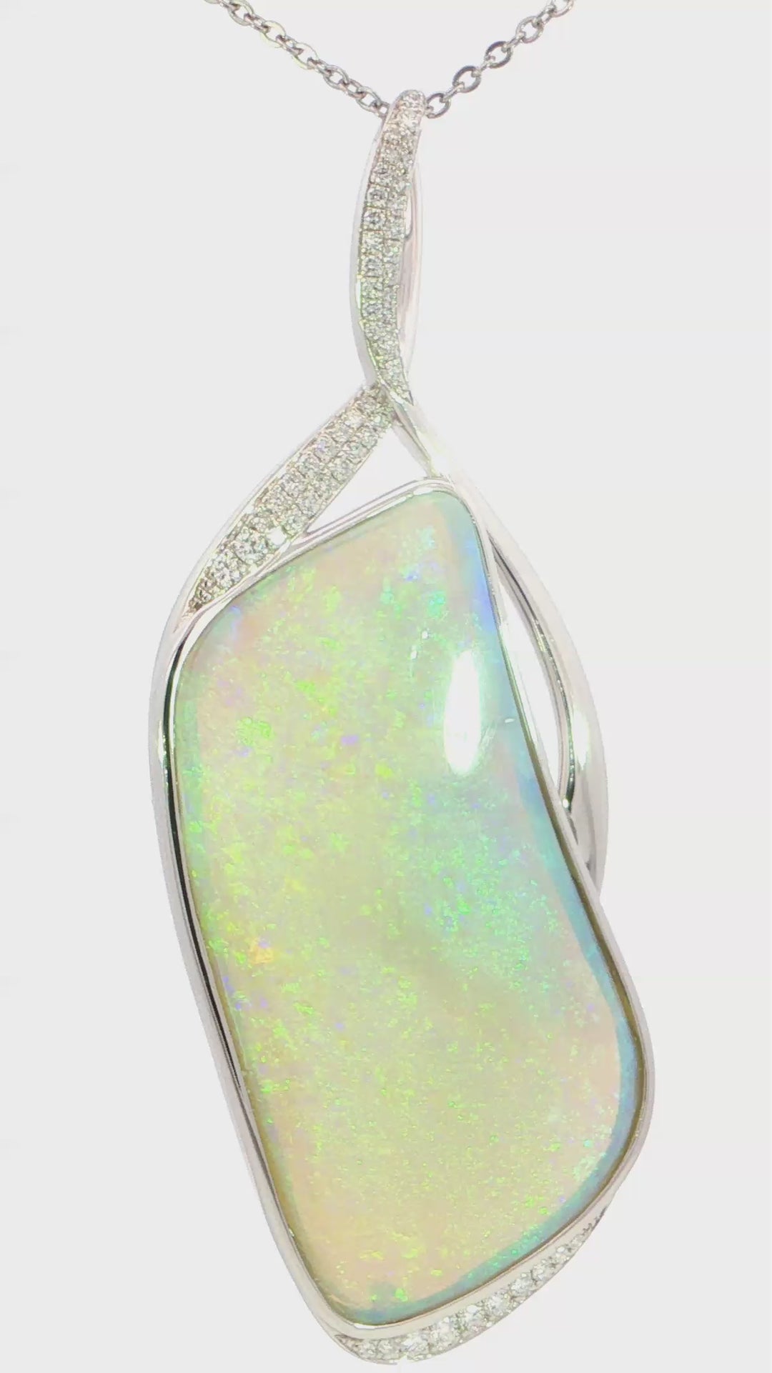 Video of a  silver pendant necklace featuring a large, irregular-shaped white opal with iridescent green and blue flashes, accented with small clear pavé stones along the bail and lower edge.