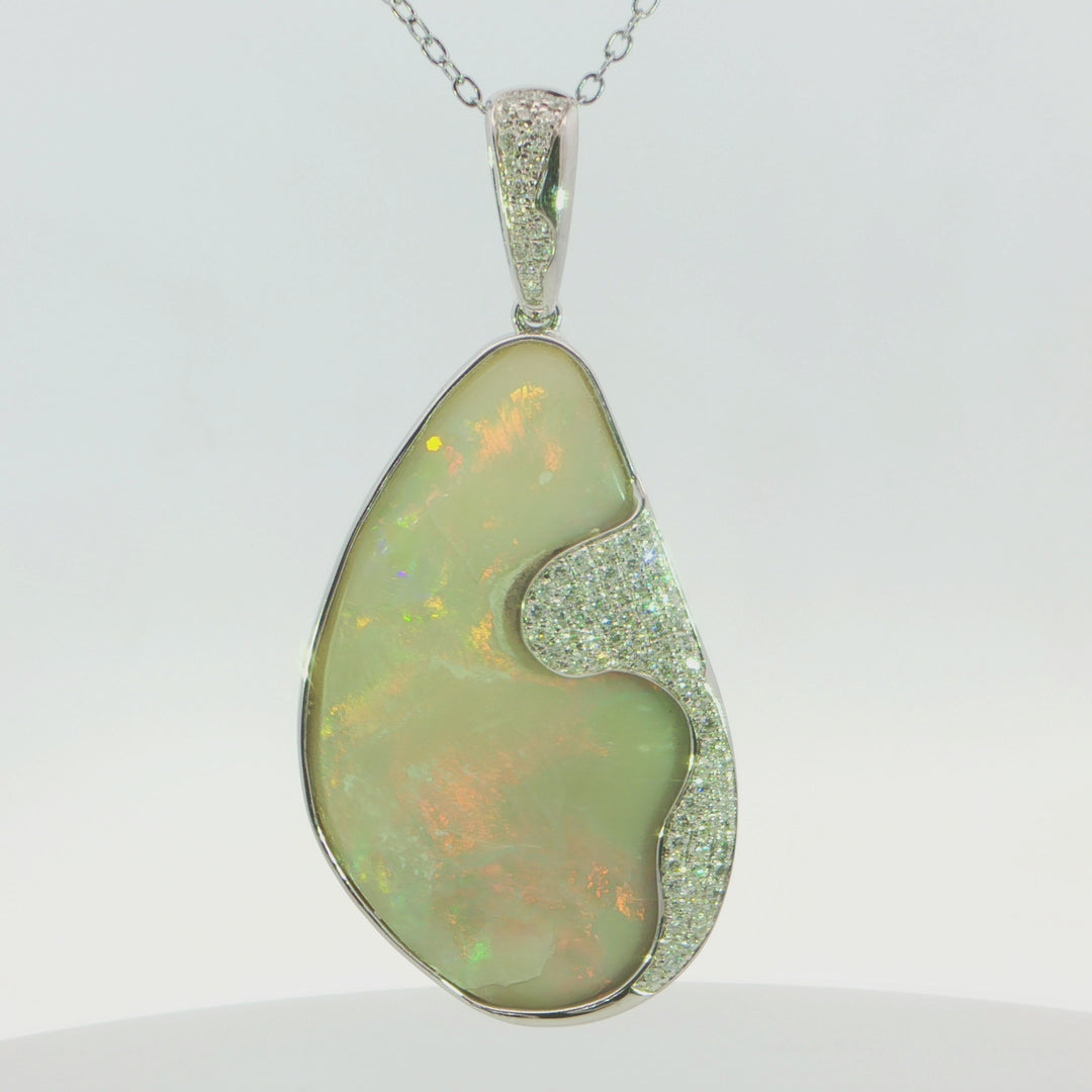 Video of a teardrop-shaped pendant necklace featuring a large iridescent opal stone with green, yellow, and orange play-of-colour, set in a silver-tone frame with pavé diamonds along the side and bail